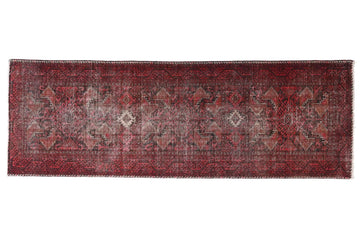 Long, narrow red rug with intricate patterns on a white background