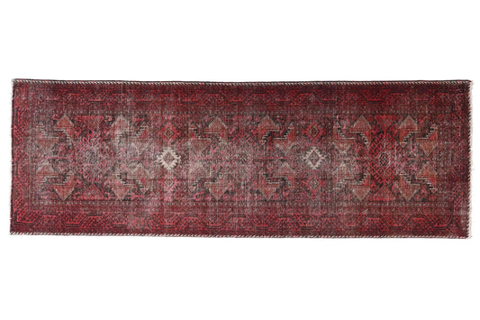 Long, narrow red rug with intricate patterns on a white background